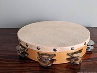 Side angle of tambourine showing wooden frame, natural drumhead and metal jingles
