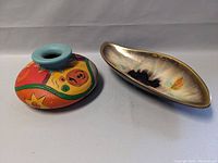 Two vases shown side by side on a white surface, one squat round and brightly painted with abstract shapes and colors, the other an elongated oval with glossy multi-color glaze.