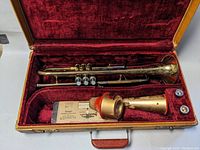 Full view of vintage brass trumpet with floral engraving inside red velvet lined case, two mouthpieces and brass accessory