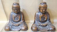 Front view of two Buddha statues in seated pose, showing detailed facial features and robes.
