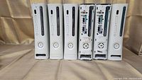 Front view of six Xbox 360 consoles showing mostly intact front panels on four and two with front panels removed or missing.