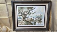 Framed lithograph showing coastal scenery with boats, dock, building and tree.