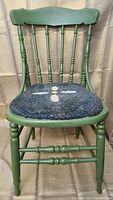 Front view of green painted antique wooden chair with padded seat showing spindle backrest and turned legs.