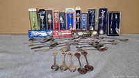 Full lot view showing spoons arranged next to displayed boxed spoons and loose spoons spread out on flat surface, approximately 40 spoons total.