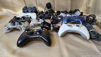 Photo showing all 12 game controllers arranged on a beige surface, highlighting variety and condition of each controller.