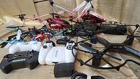 Full view of multiple remote helicopters and drones with controllers and spare parts, showing variety in size and color