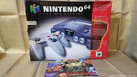Photo showing the front of the Nintendo 64 console box with controllers pictured and a mostly red background, box edges show wear and damage.