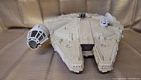 Front and side view of the Millennium Falcon toy showing cockpit and front details on beige surface.