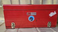 Closed red metal Craftsman toolbox with stickers on front and secured latches