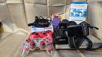 Various electronics arranged including Nikon Coolpix camera, Nintendo Wii console, two wired game controllers, battery chargers, a box of Konica camera film, and Ethernet cables.