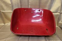 Top view of red tractor seat showing curved shape and multiple holes in seat base.