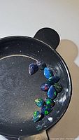 Black circular container holding 11 pear-shaped faceted Ethiopian black opal gemstones showing vibrant rainbow flashes.