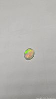 Oval cabochon natural Ethiopian opal showing bright green and orange rainbow flashes on a pale body.