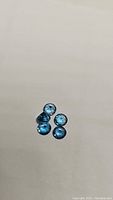 Five deep blue London Blue Topaz round cut gemstones laid out on a neutral background