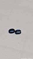 Matched pair of oval cut London blue topaz gemstones with deep blue color, photographed on neutral background showing facets and clarity.