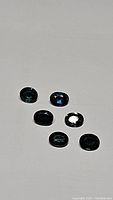 Six oval cut natural sapphires showing multicolored blue and green hues laid on white background.