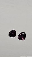 Two small heart-shaped deep red-pink-purple sapphires on a white background, showcasing their cut and color.