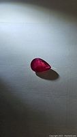 Pear-shaped red ruby resting on white surface under ambient light