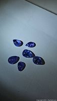 Six loose pear-shaped purple tanzanite cabochon gemstones on white background, showing color, size, and natural inclusions.