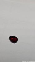 Close-up photo of natural cherry red garnet gemstone, pear-shaped cabochon cut, showing deep red color and polished surface.