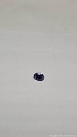 Close-up photo of deep purple blue oval cut tanzanite gemstone on neutral background showing clarity and cut facets.