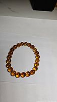 Photo showing the circular arrangement of polished amber beads on an elastic band, highlighting the semi-transparent quality and warm amber hues.