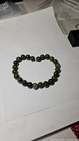 Photo of a natural green jade bead bracelet laid out flat on white paper, showing round green beads with some color variation.