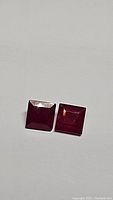 Two square cut red rubies on plain white background, top-down view