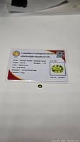 Certification card from Chanthaburi Gemological Laboratory with details including type: Natural Grossular - Andradite Garnet, weight: 0.64 ct, color: Yellow-Green, cut: Oval Mixed, hardness 7-7.5, dimensions 4.37x5.93x1.07 mm, dated 4 Nov 2023