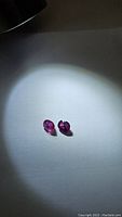 Photo of two loose pink-blue multicolored sapphires under light showing colors and facets distinctly