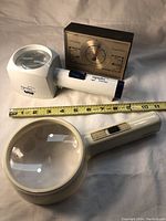 Magnifiers and barometer side by side with measuring tape for scale
