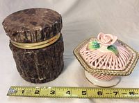 Two unique containers placed side by side on a white surface with a measuring tape showing length approximately 4 inches for the alabaster container and 5 inches wider pink metal container.