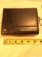 Black leather carrying case for Agfamatic Pocket Autoset camera with measurements shown by tape measure.