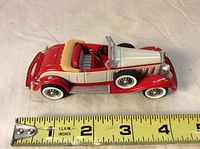 Diagonal top-side view of the Cadillac roadster ornament with measuring tape showing length of approximately 4.5 inches.