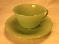 Front view of a pale green Jadeite cup seated on matching saucer