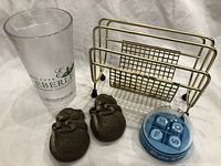 Photo showing two Sandicast squirrel sculptures, plastic water glass labeled 'Hotel Eberle', blue and clear plastic Shake and Make Words game, and brass-colored metal desk letter holder.