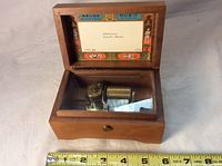 Open-top view of Reuge wooden music box showing metal music cylinder and comb, with label inside lid listing tunes