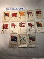 Full set of 13 vintage Sovereign Cigarettes flag silk inserts laid out with measuring tape for scale, showing variety of flags.
