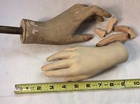 Two plaster mannequin hands laid side by side with detached fingers visible near the cracked hand and a measuring tape for scale showing about 8 inches in length.