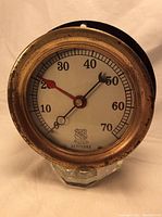 Front view of circular brass pressure gauge with white dial and black needles, shows scale from 0 to 70 and brass housing wear.