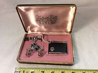 Open set showing lighter, tie bar, and cuff links inside pink felt-lined case with silk lid.