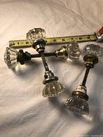 Three vintage glass door knob sets connected by metal shafts, showing varying metal finishes and wear, measuring about 8 inches in length.