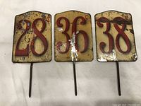 Three vintage metal produce price signs showing 28¢, 36¢, and 38¢ with wear and rust.