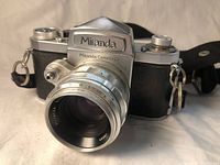 Front angled view of vintage Miranda SLR camera with attached 50mm f/1.9 lens. Camera body is silver and black with strap.