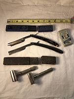 Top view of two straight razors, two safety razors, razor boxes, and Gillette blade pack with measuring tape showing scale
