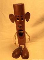 Front view of the teak pipe cleaner holder with anthropomorphic face, rope arms, and wooden feet, standing upright.