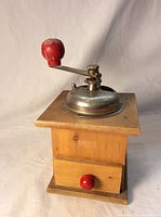 Front side view of the wooden coffee grinder showing the metal grinder top and red handle knob.