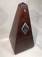 Front side view of wooden Wittner metronome showing pyramid shape and logo.