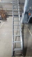 Full length view of one aluminum extendable ladder laid out flat on the ground showing rungs and side rails.