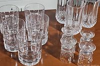 Photo shows a mix of short whiskey glasses, tall highball glasses, and small stemmed wine glasses in clear glass with decorative patterns.